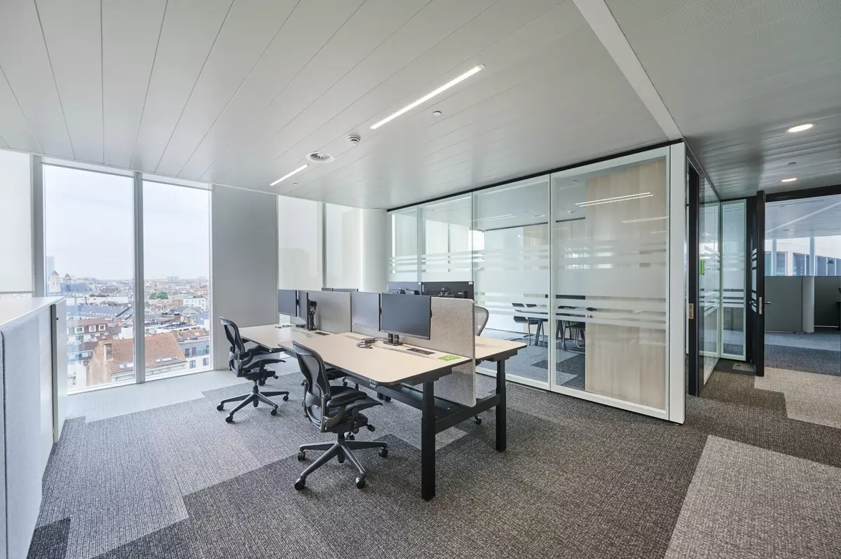 Een modern kantoor ingericht met ergonomische witte bureaus, grijze scheidingspanelen en zwarte bureaustoelen.