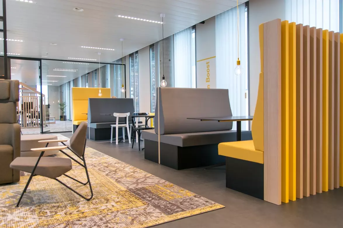 Bureau moderne avec alcôves jaunes et grises, suspensions industrielles et tapis à motifs.