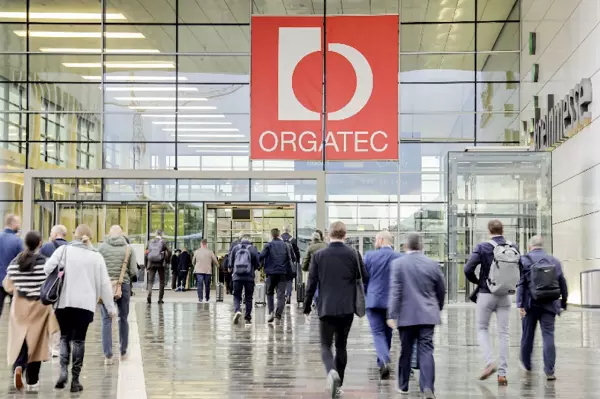 Mensen lopen naar de ingang van een ruim gebouw met een rood bord met de tekst "Orgate