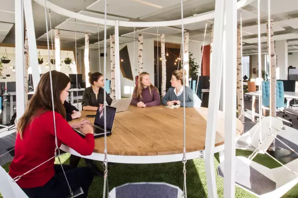 Vergaderruimte met ronde houten tafel en schommelstoelen in een open kantooromgeving met natuurlijke lichtinval