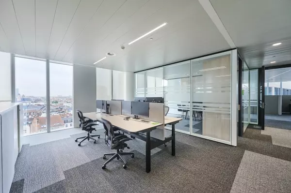 Een modern kantoor ingericht met ergonomische witte bureaus, grijze scheidingspanelen en zwarte bureaustoelen.